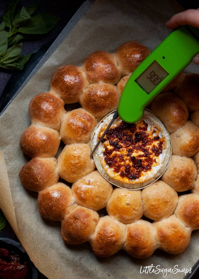 Green food thermometer being used to test that dough balls are cooked through