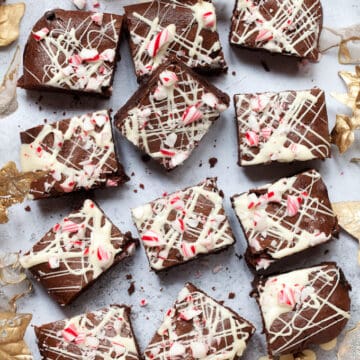 Squares of Candy Cane Brownies topped with white chocolate and chunks of candy cane on a grey worktop