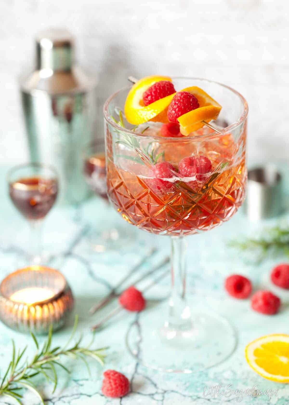 A winter version of aperol spritz with sloe gin and rosemary. Garnished with orange and raspberries