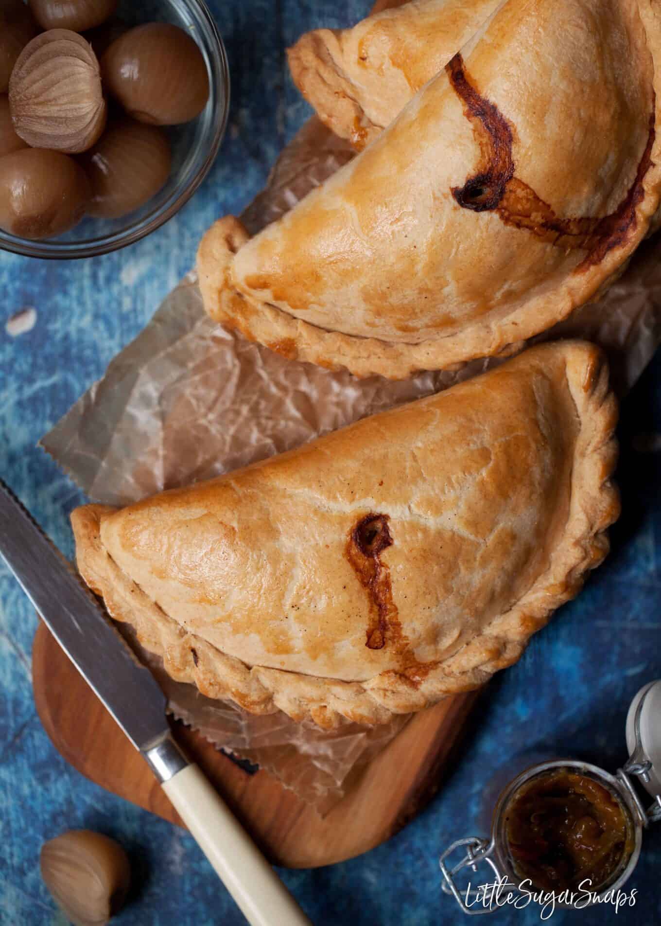 Beef pasties on a wooden serving platter with pickled onions and relish