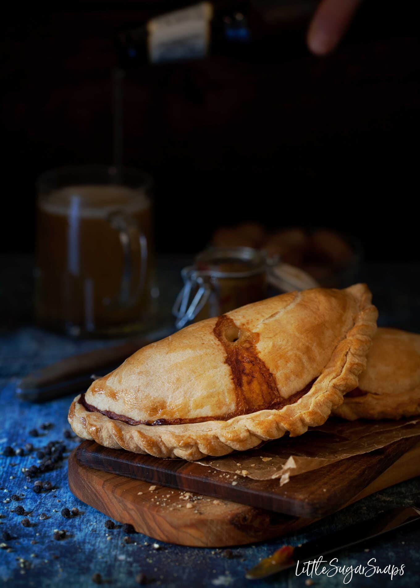 Beef pasties on a wooden serving platter with pickled onions and relish.