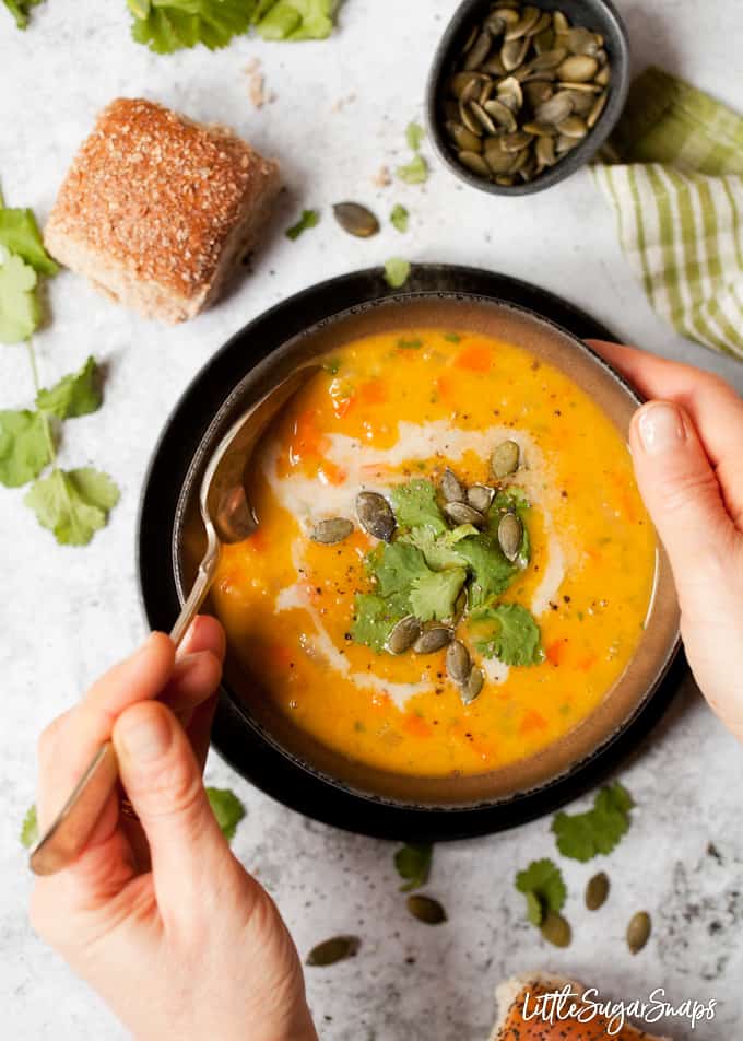 Person with hands around a bowl of vegan carrot soup about to take a spoonful.