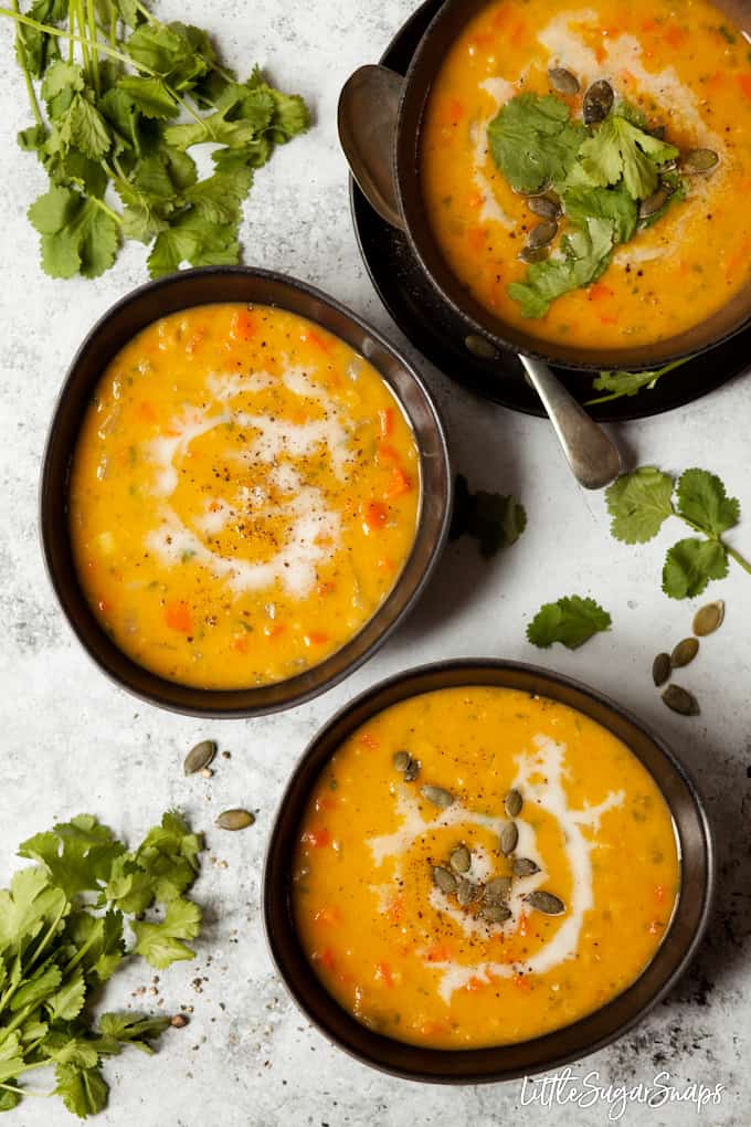 Three bowls of vegan carrot soup garnished with fresh coriander and pumpkin seeds