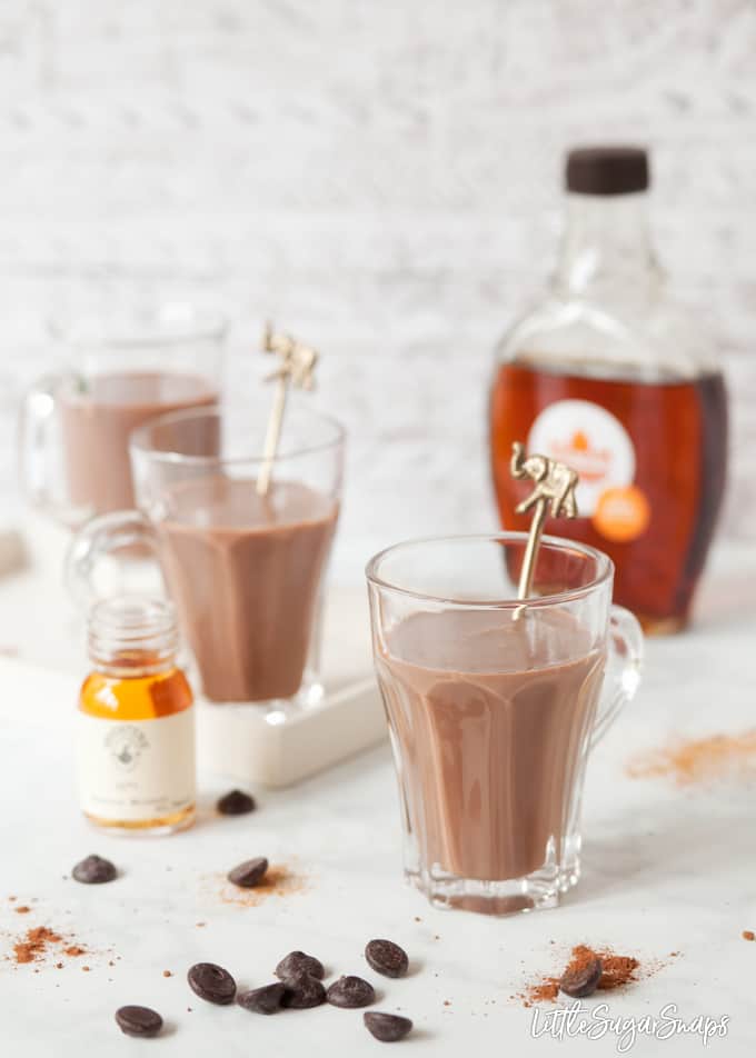 Bourbon Hot Chocolate in glasses with bottles of bourbon and maple syrup alongside.