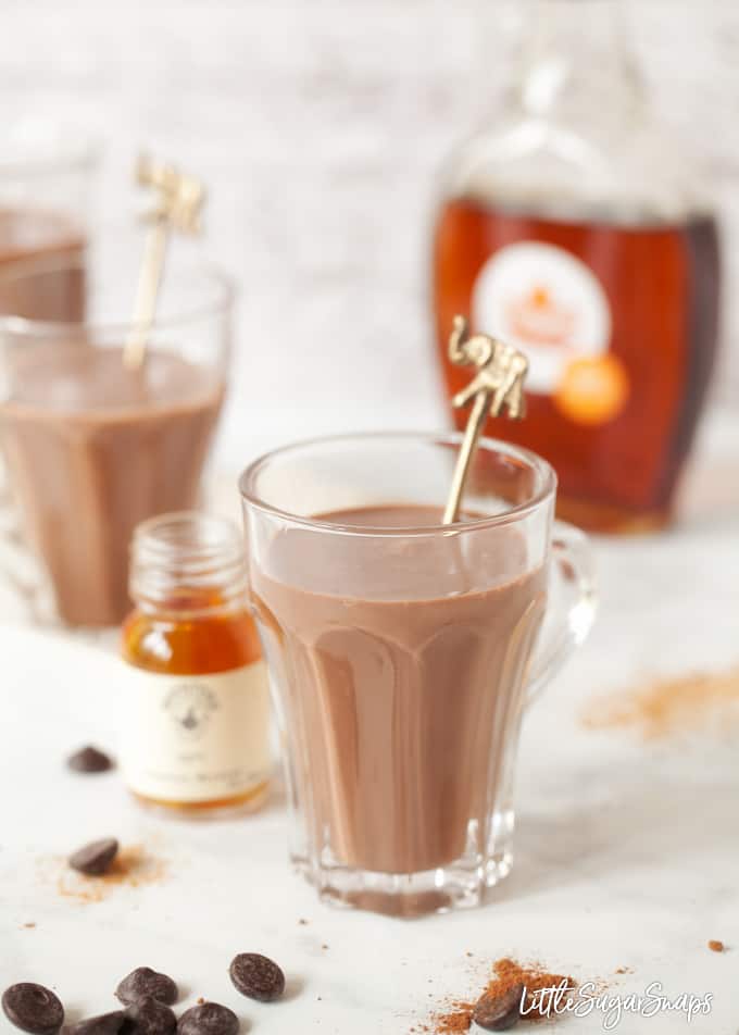 A glass of hot chocolate with bottles of maple syrup and bourbon alongside