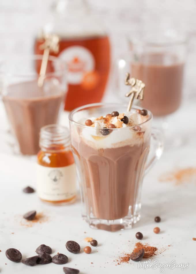 Hot chocolate topped with cream and sprinkles with bottles of bourbon in shot