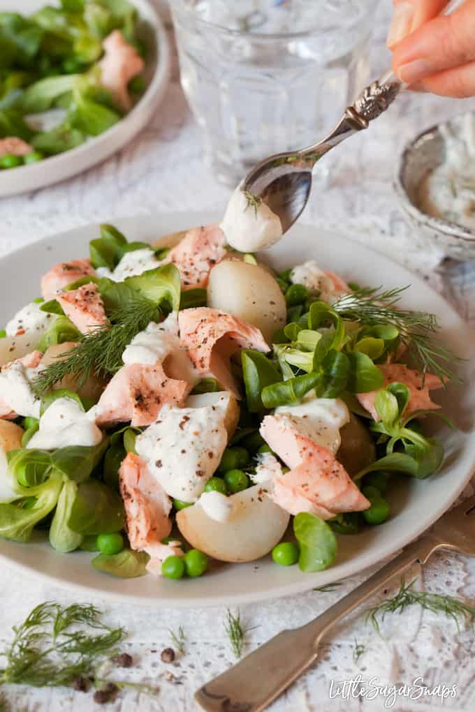 Person spooning salad dressing over a salmon and potato salad.
