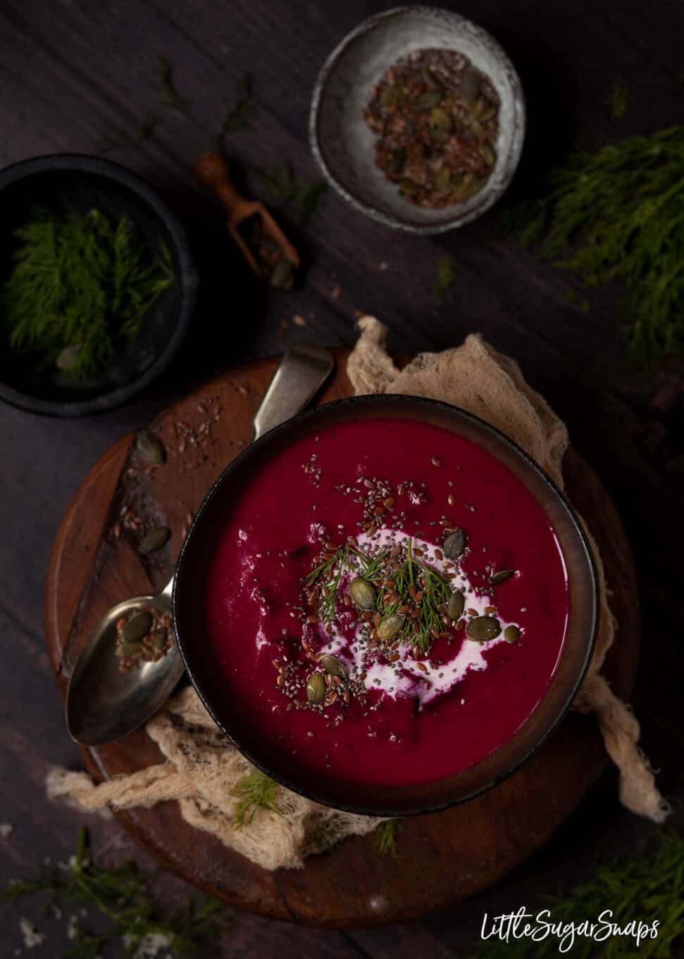 A bowl of beet soup with cream, dill and pumpkin seeds. 