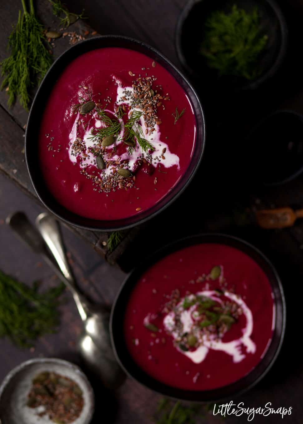 Two bowls of beetroot and horseradish soup with cream and seeds as a garnish. 