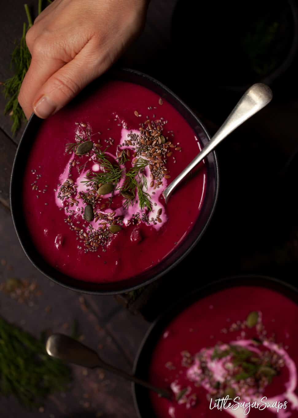 A hand reaching in to take a bowl of beetroot and horseradish soup.
