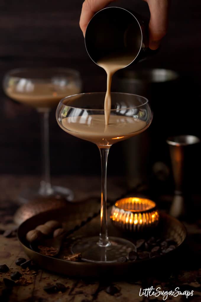 Pouring a creamy alexander cocktail into a glass.