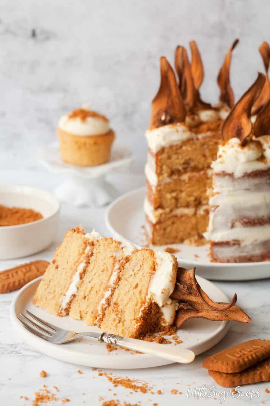 A slice of Lotus Biscoff cake on a plate with the cut cake behind.