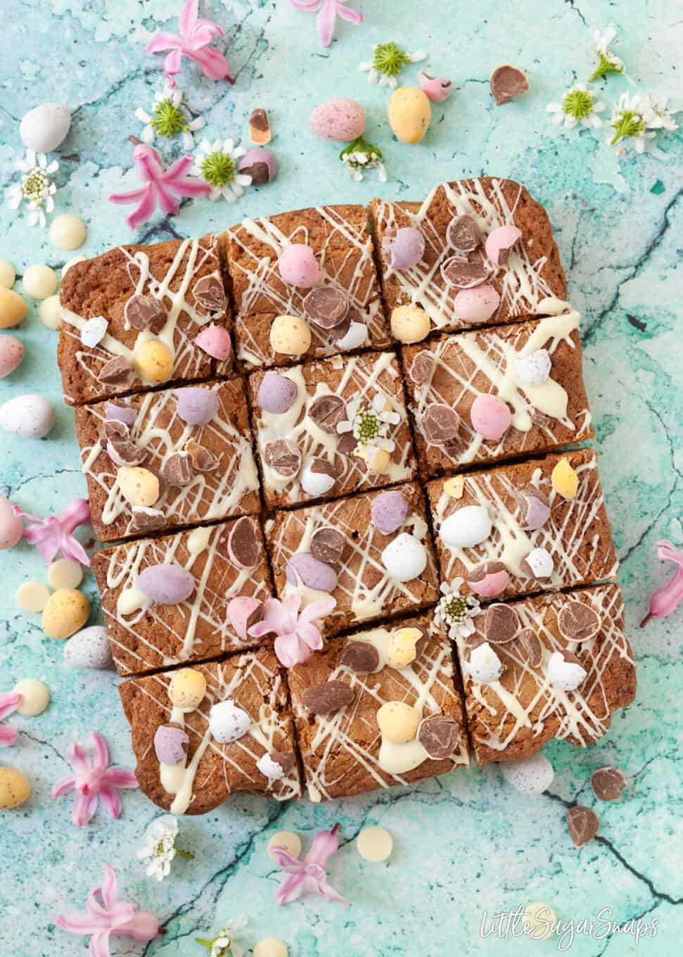 Squares of easter themed brown butter blondies with coconut on a blue board. 