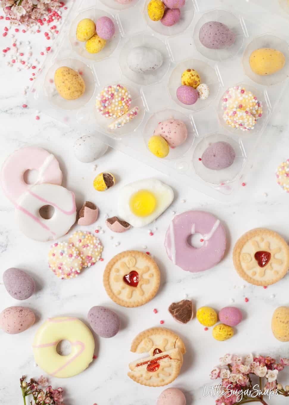 Miniature biscuits, chocolate eggs and sprinkles on a marble table top assembled for a homemade easter egg recipe