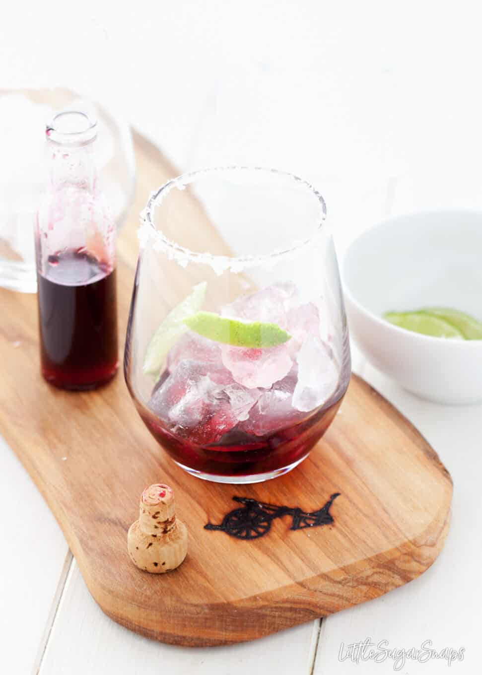 Hibiscus syrup poured into a glass with lime wedges and ice in the glass. 