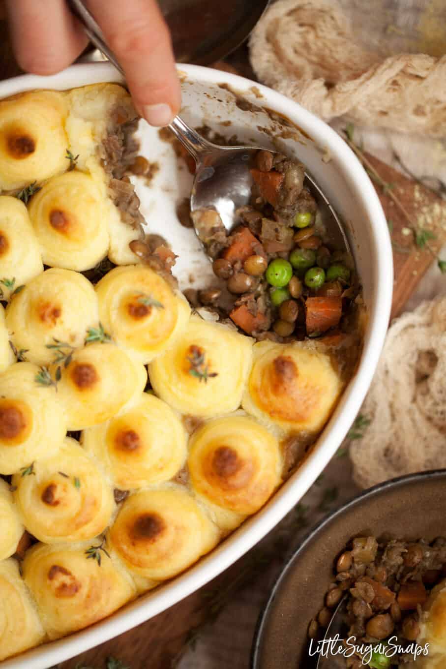 Person serving potato topped vegan lentil shepherds pie into bowls.