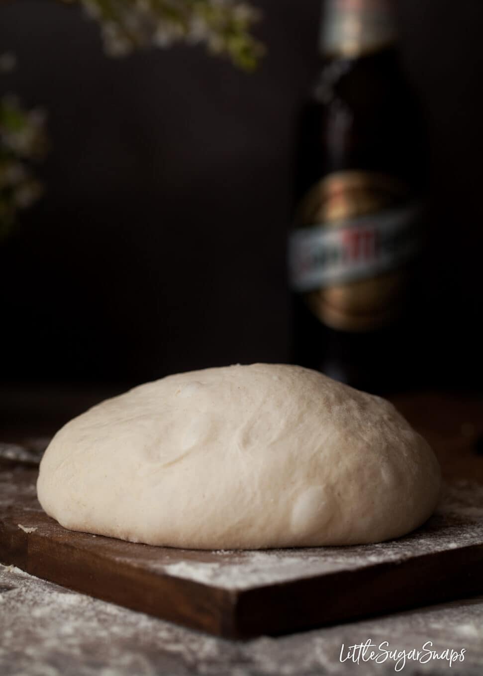 Beer pizza dough ready to cut and roll out. On a wooden board dusted with flour with a bottle of beer in the background