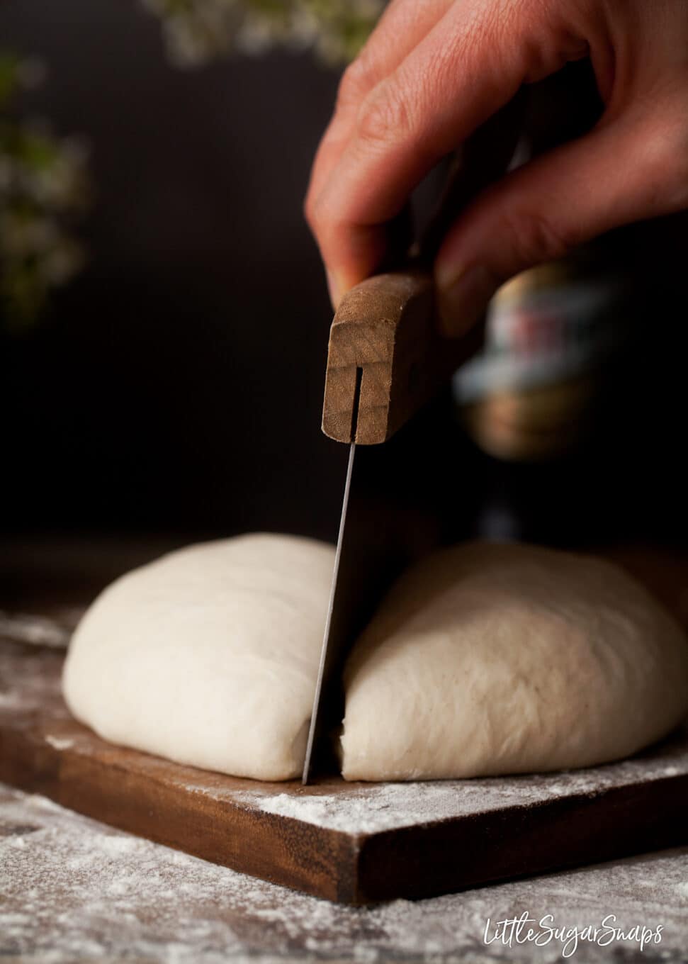 Slicing small batch beer pizza dough in half using a dough scraper.