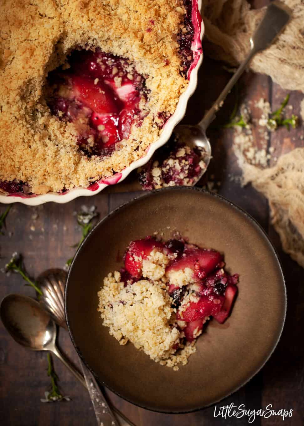 Blackcurrant crumble with apple served from a large round oven dish into a bowl.
