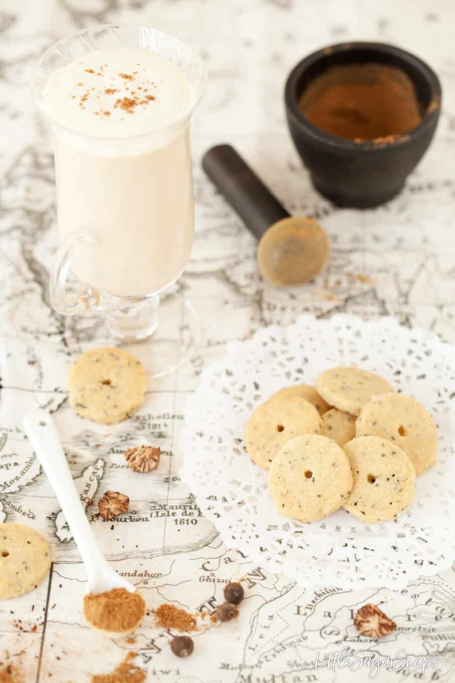 A chai latte with a few miniature biscuits on a paper doiley. 