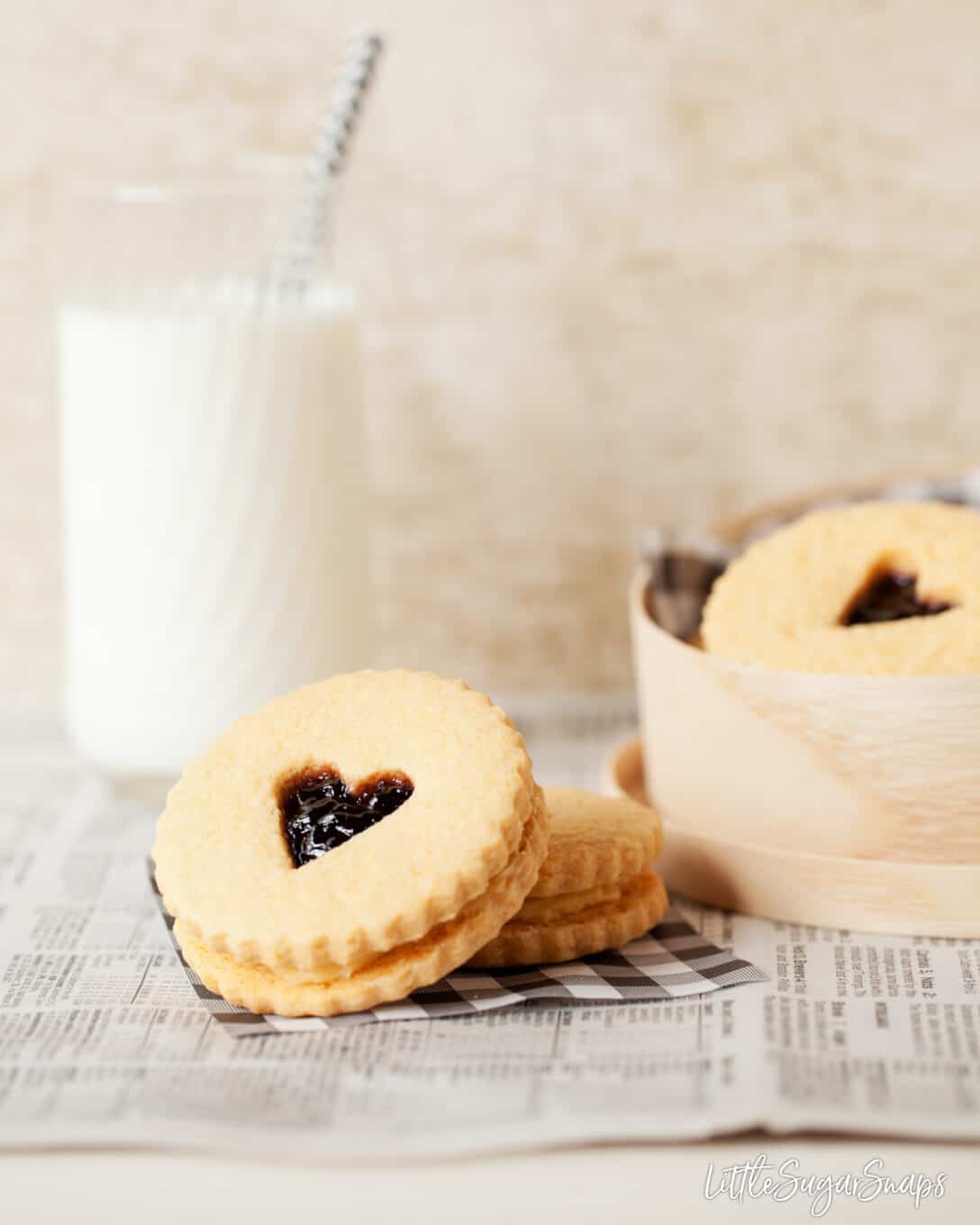 A box of jam and buttercream filled biscuits with heart cut outs served with milk