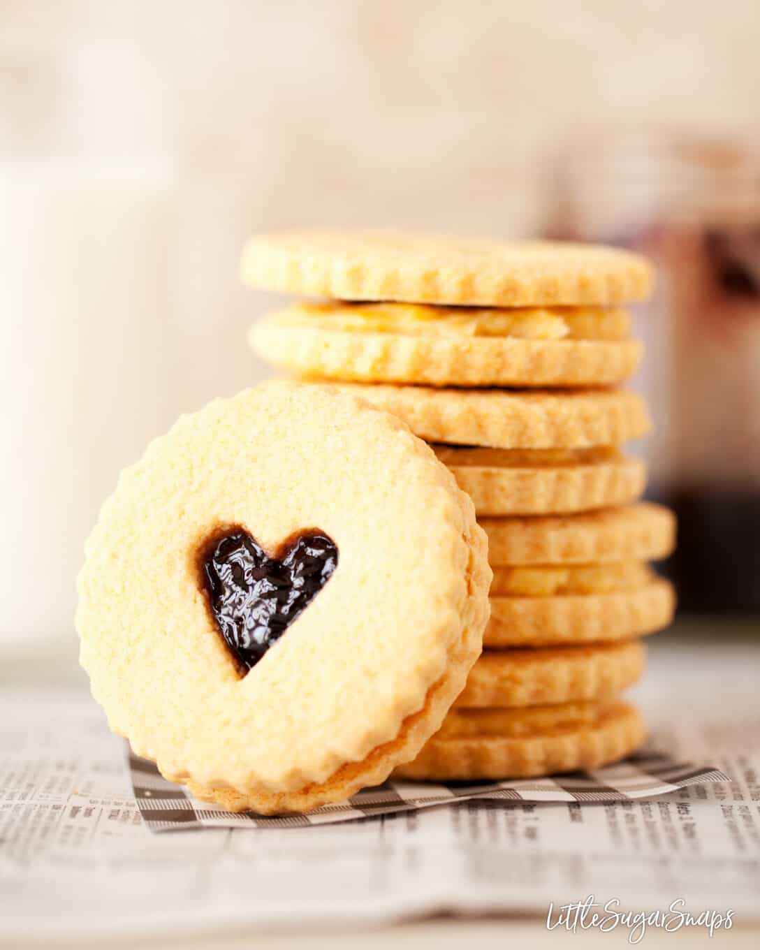 A stack of Custard Creams Biscuits with jam in the middle too. A love heart is cut out of one biscuit that is one it's side facing the camera angle.