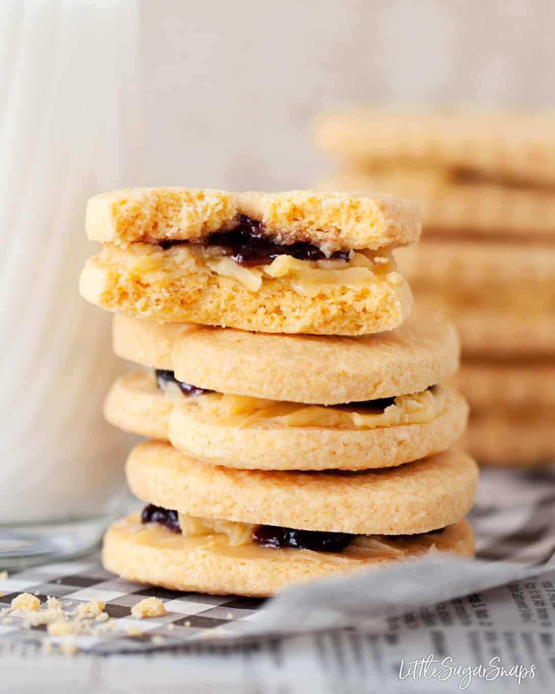 Stacked custard creams biscuits with cream filling and jam in the centre. Top one is bitten into
