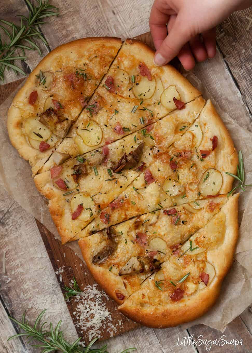 Cooked pizza topped with potato, bacon, artichoke and rosemary. Cut into slices.