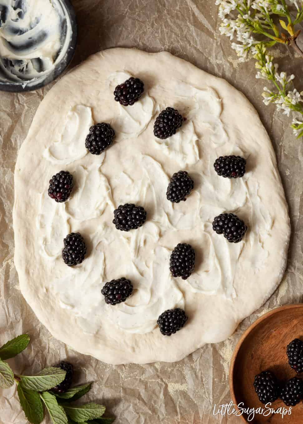 Blackberries scattered onto sweetened mascarpone cheese spread on a pizza base