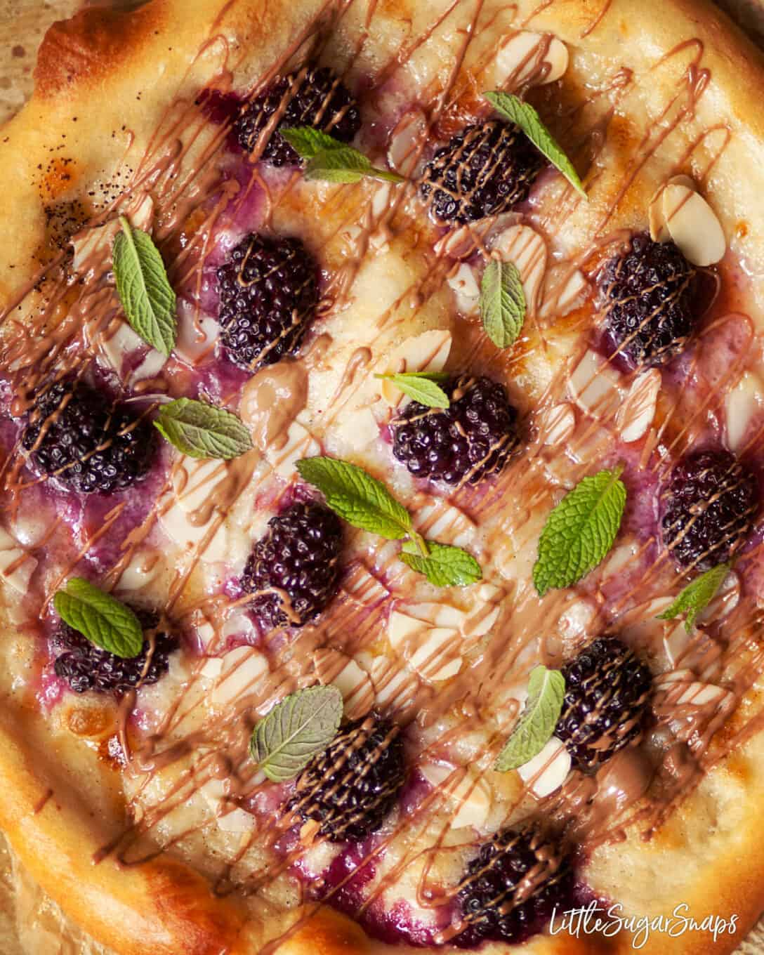 Close up of sweet dessert pizza topped with blackberries, chocolate drizzle and fresh mint.
