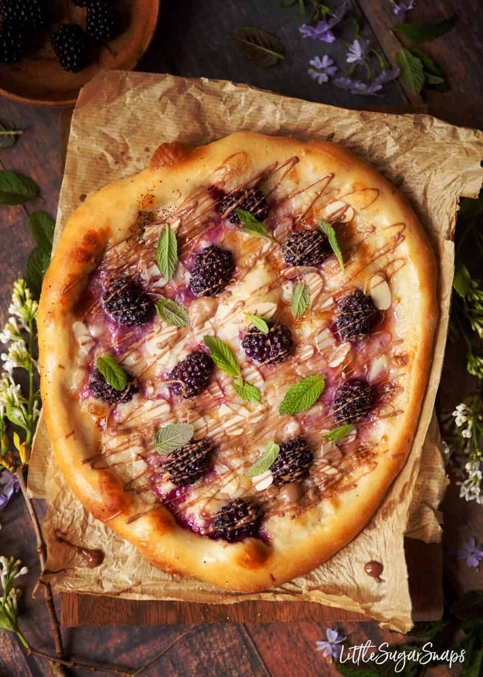 Sweet pizza topped with mascarpone, blackberries, milk chocolate drizzle, almonds and mint leaves.