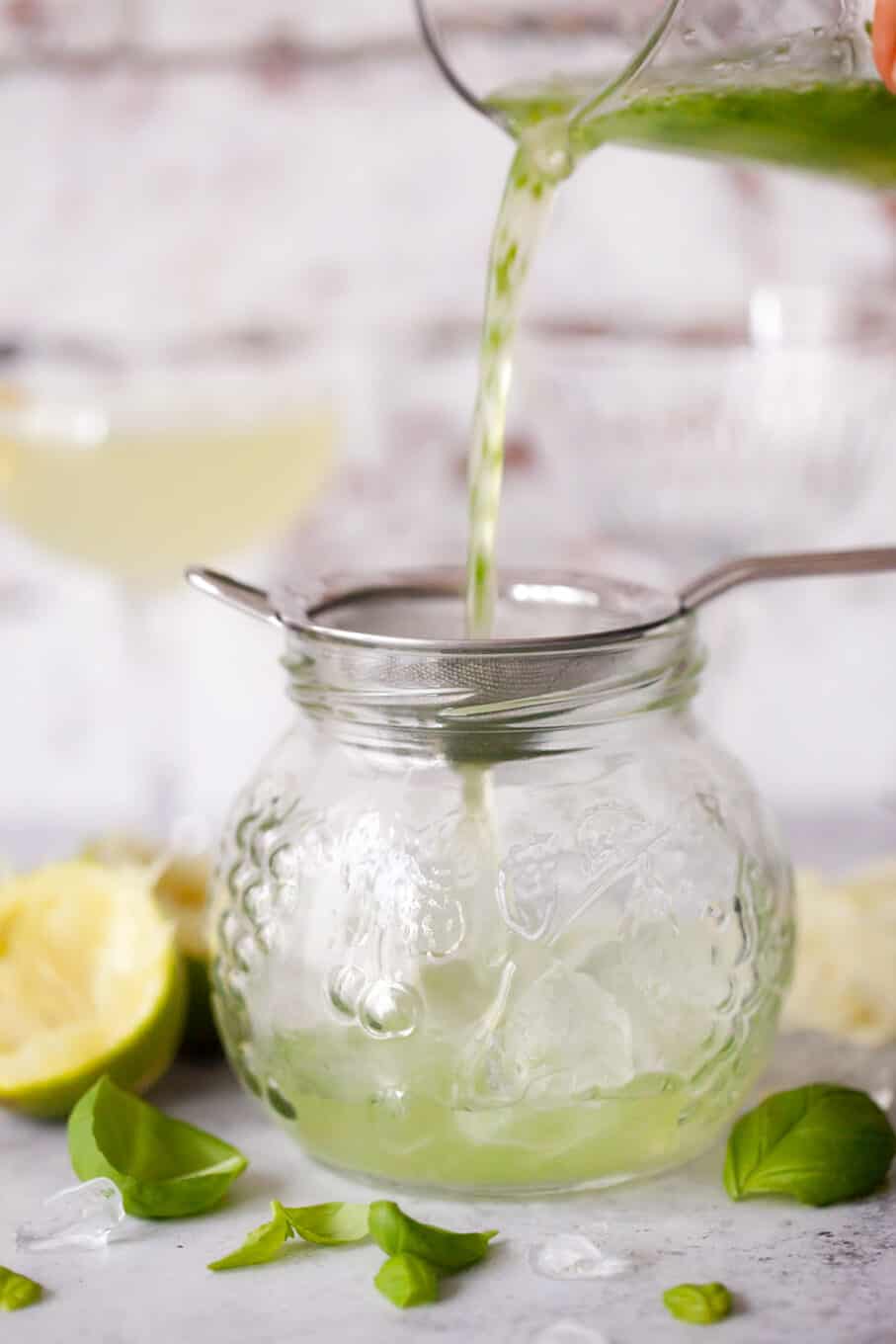 straining green chartreuse cocktail ingredients through a sieve