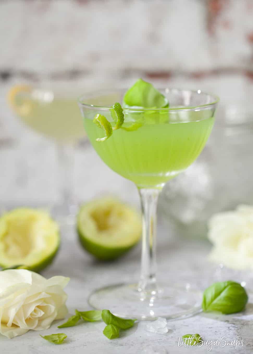 A basil, lime and green chartreuse cocktail garnished with lime zest and basil.
