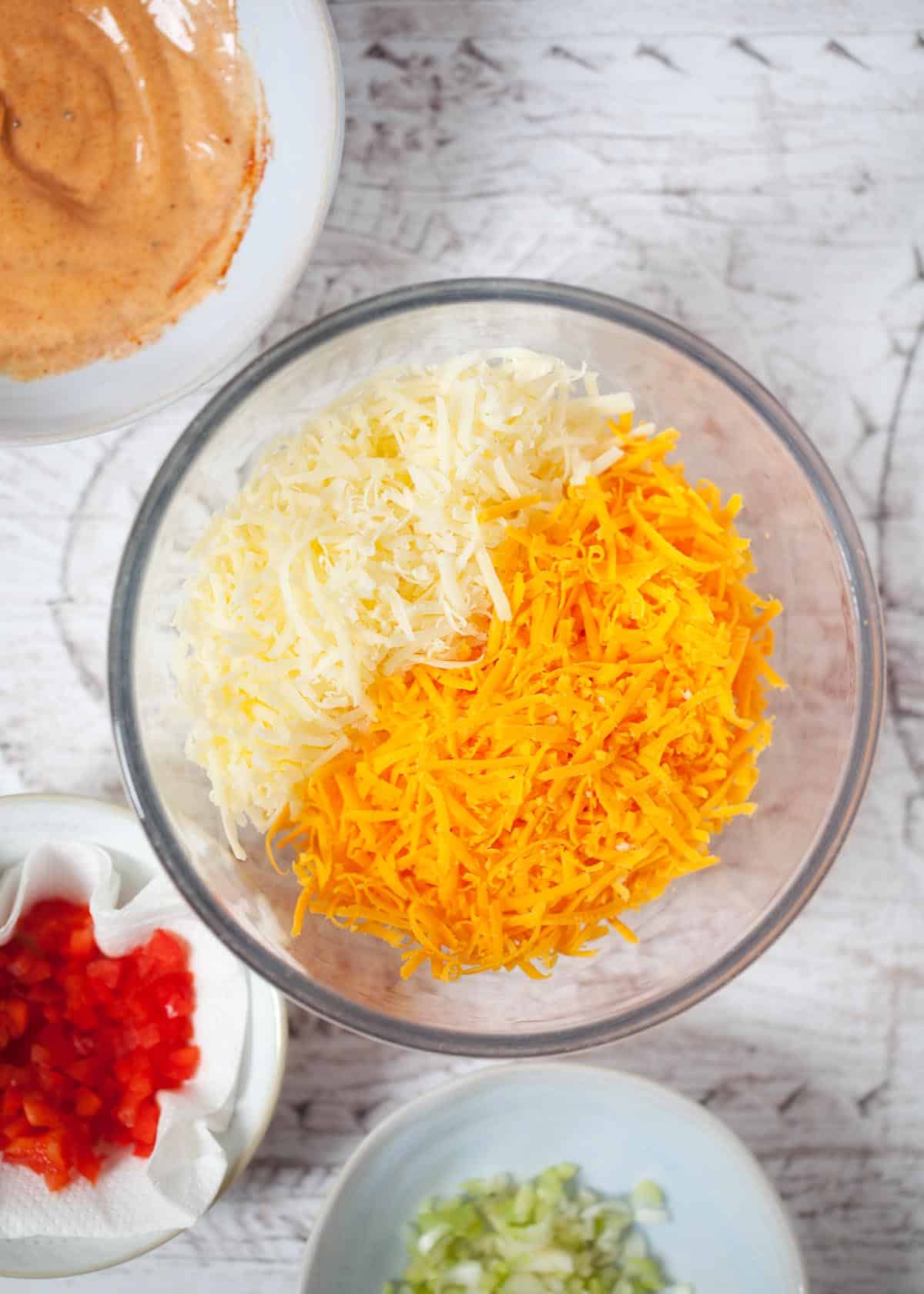 Two types of cheese (cheddar and red Leicester) finely grated into a bowl 