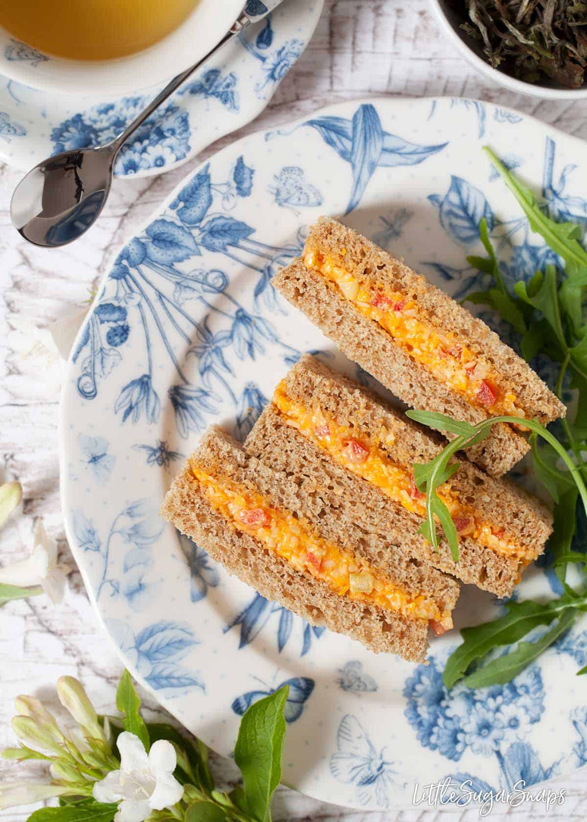 Three cheese savoury sandwiches are sitting on a pretty blue and white plate.