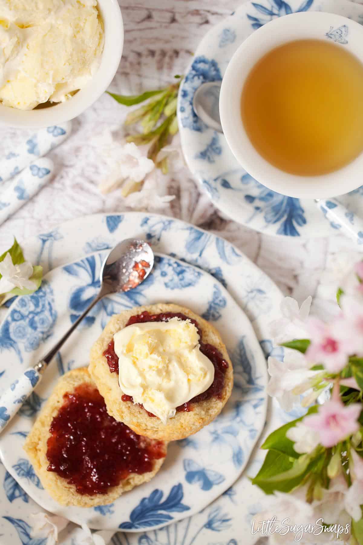 Overhead view of a scone topped with jam and clotted cream, served as afternoon tea