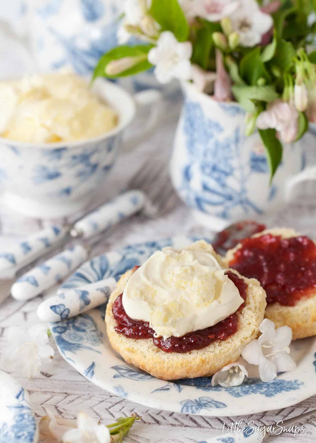 An English scone split open and topped with raspberry jam and clotted cream. 