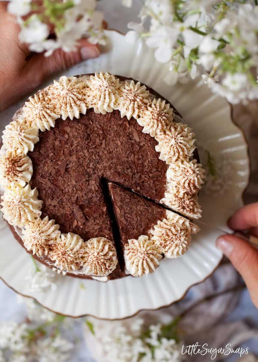 Person cutting into a cake topped with cream and chocolate flakes. 