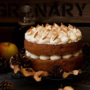 A 2 layer cinnamon and apple cake sandwiched together with buttercream and decorated with dried apple and ground cinnamon. Presented on a wire rack with slices of apple and pine cones around it