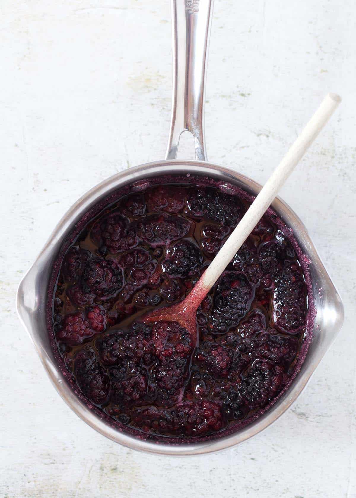 Blackberry compote in a saucepan with a wooden soon in it