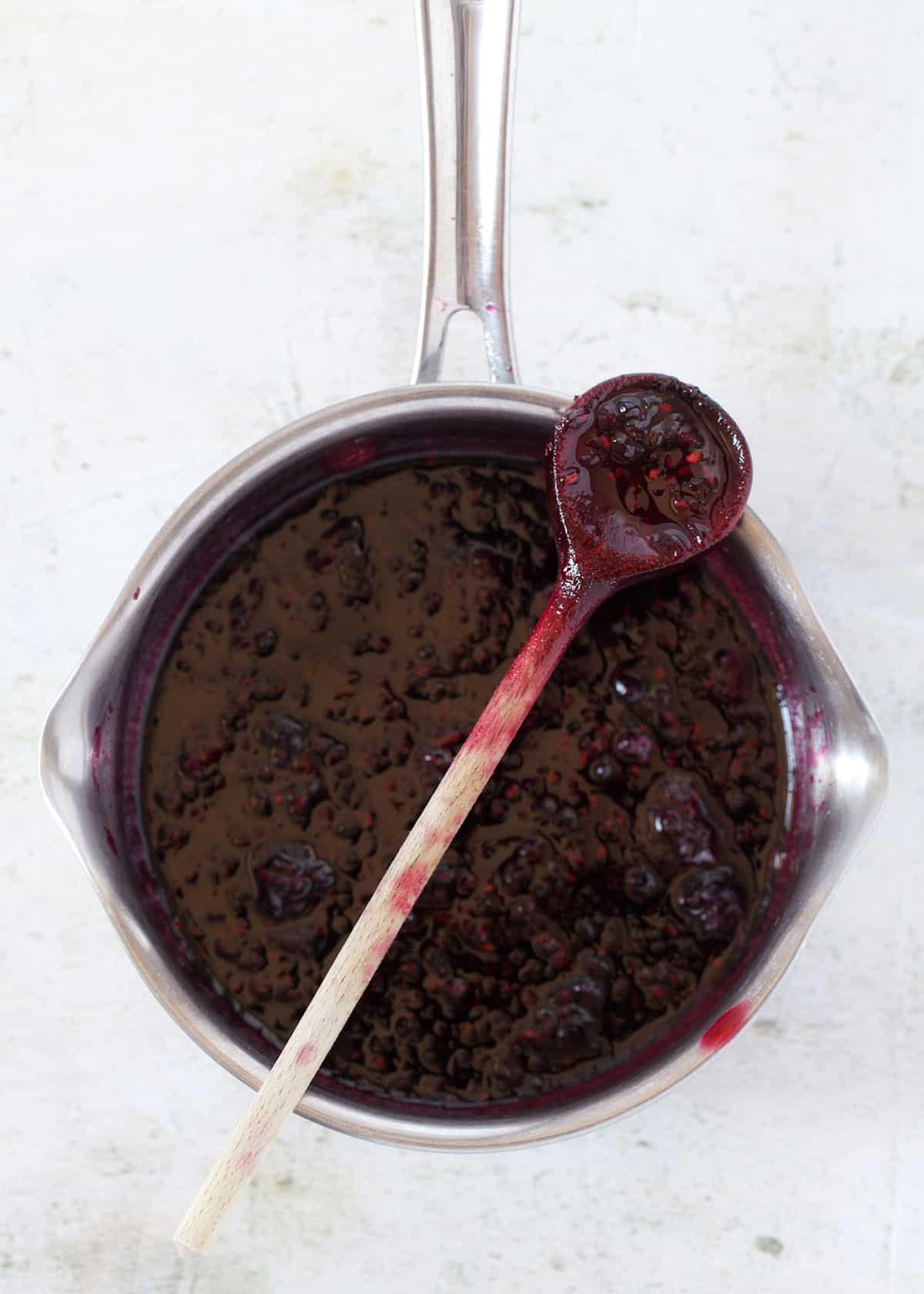 a saucepan containing blackberry compote with a small wooden spoon resting across it