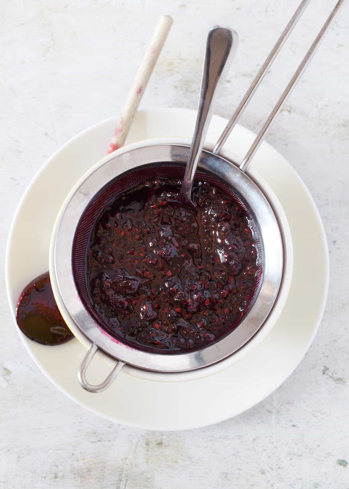 Blackberry compote being strained through a mesh sieve