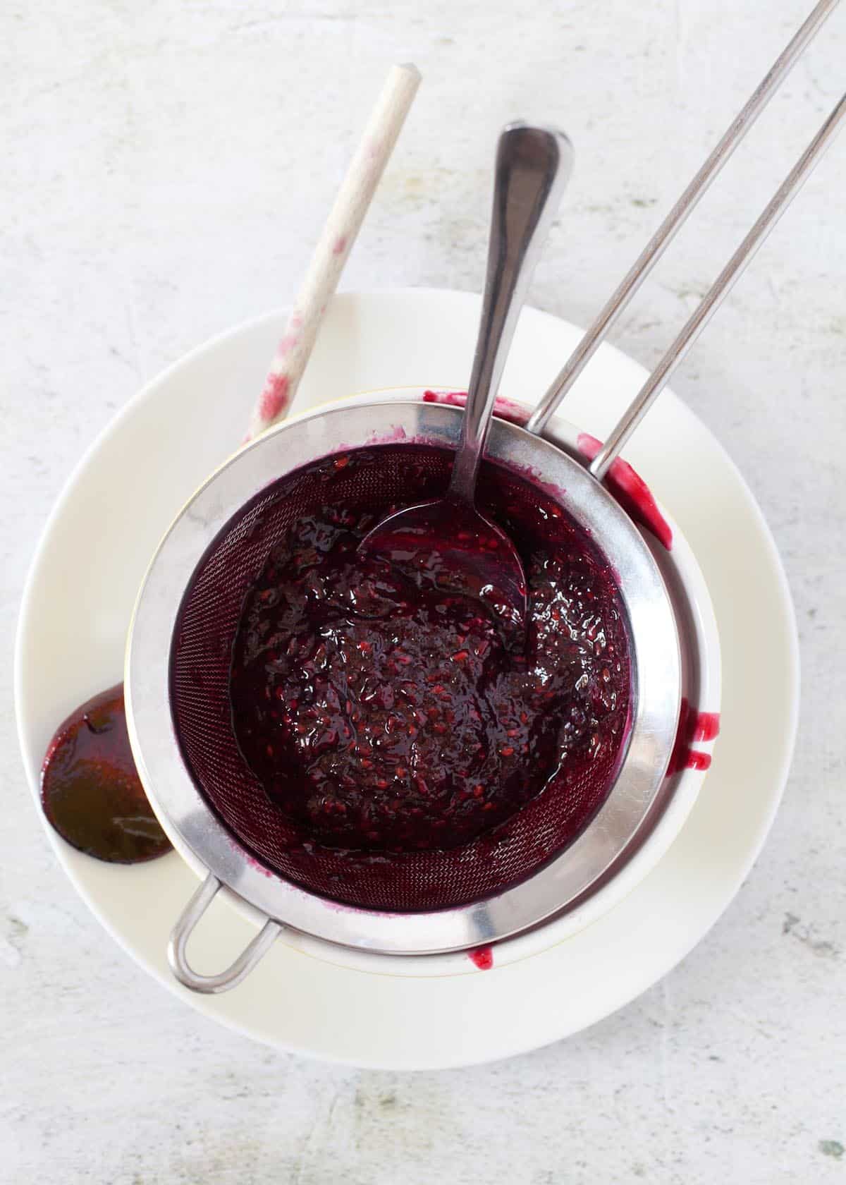 Blackberry compote being strained through a sieve