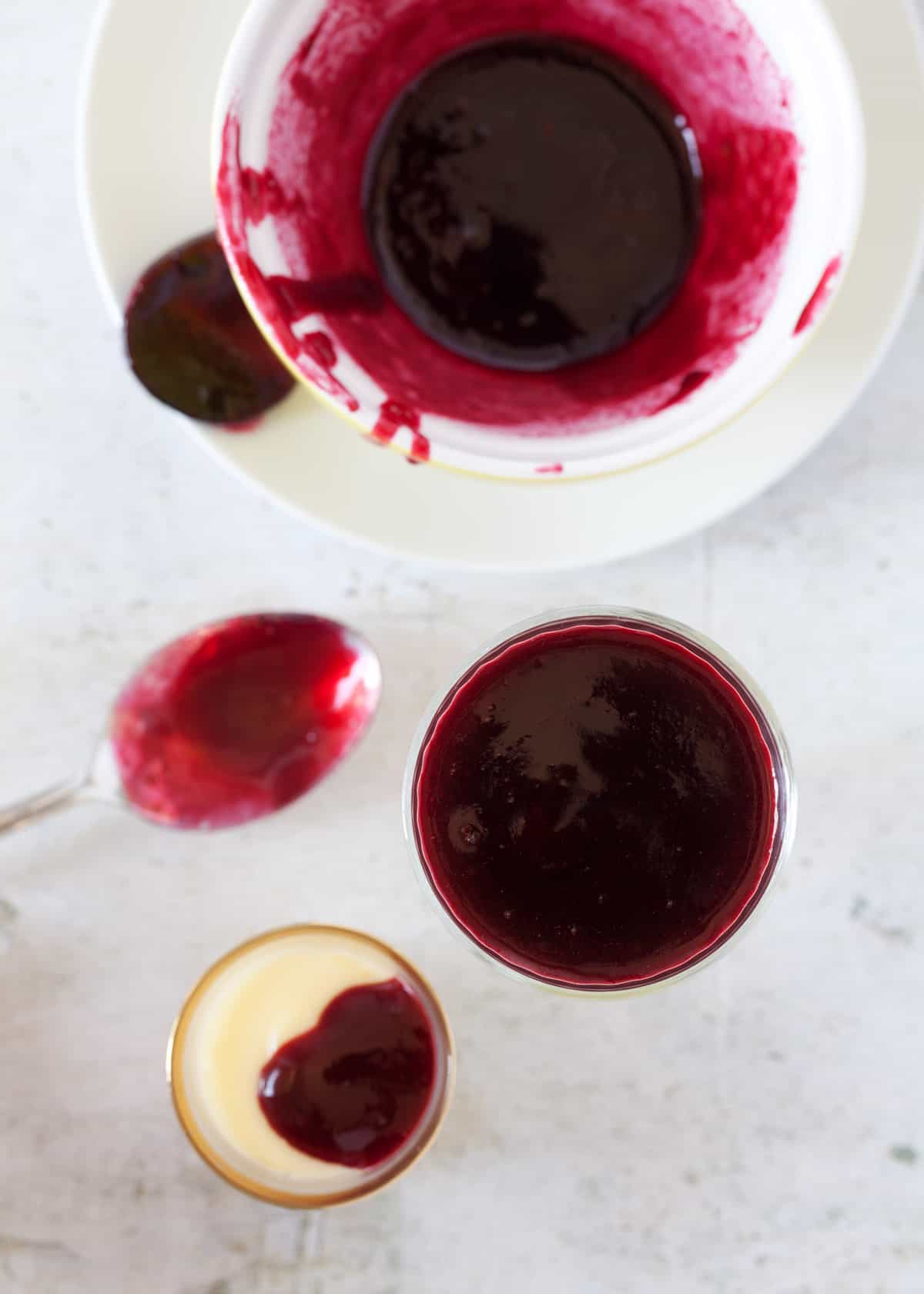 Spooning blackberry compote over lemon posset in individual glasses