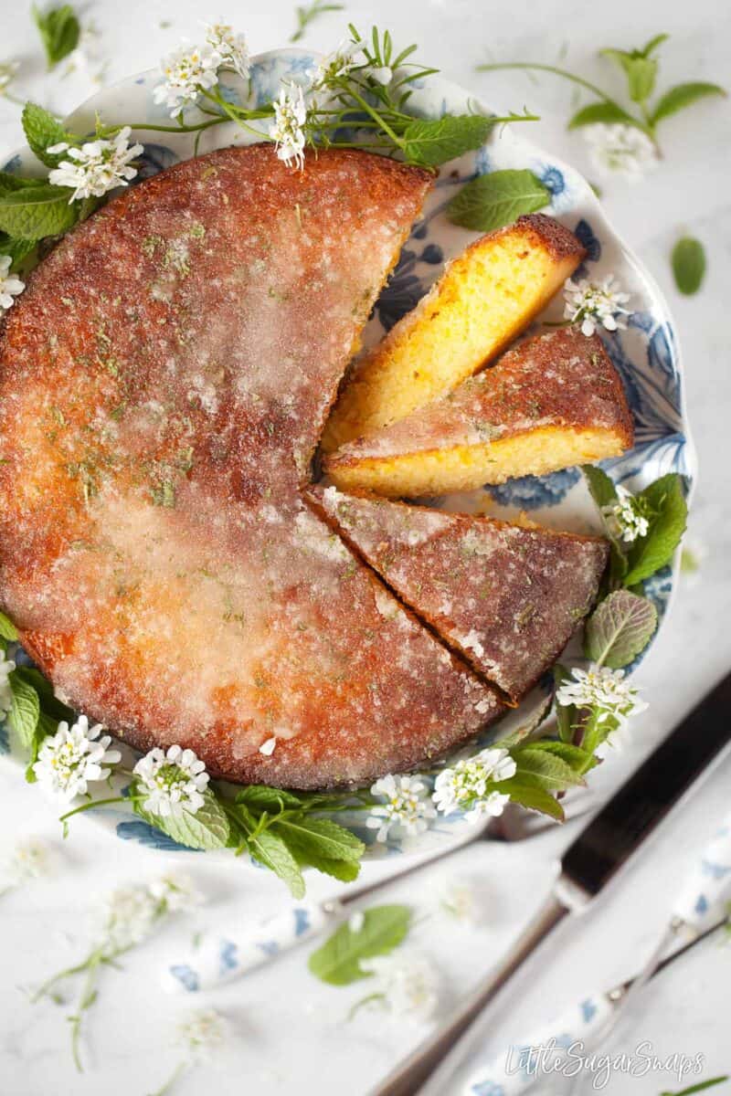 Orange semolina cake with orange and mint drizzle on a cake stand with slices cut.