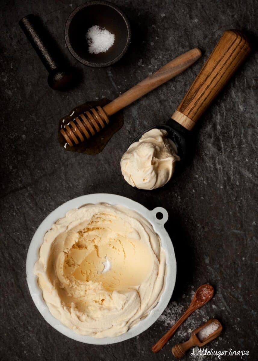 Salted honey ice cream part scooped out of a tin with ingredients in shot