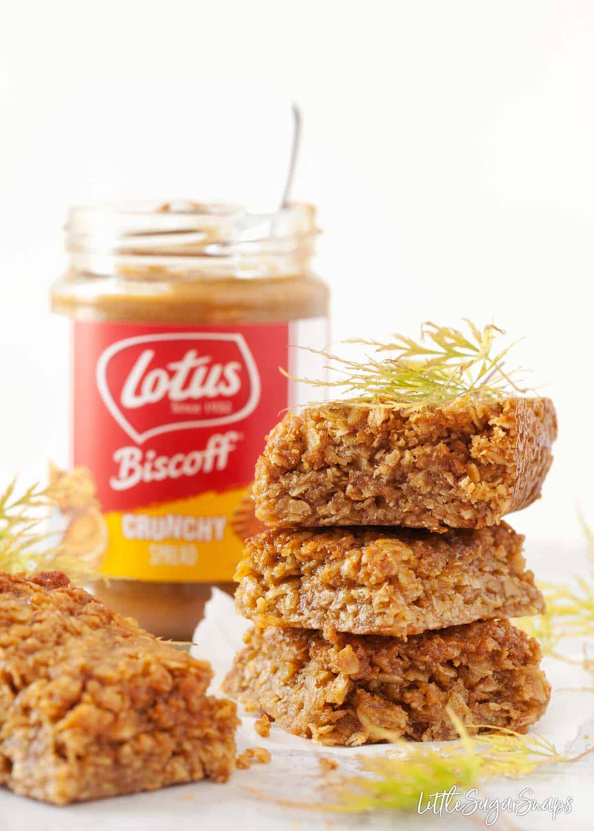 Squares of flapjack stacked in front of a jar of Biscoff spread