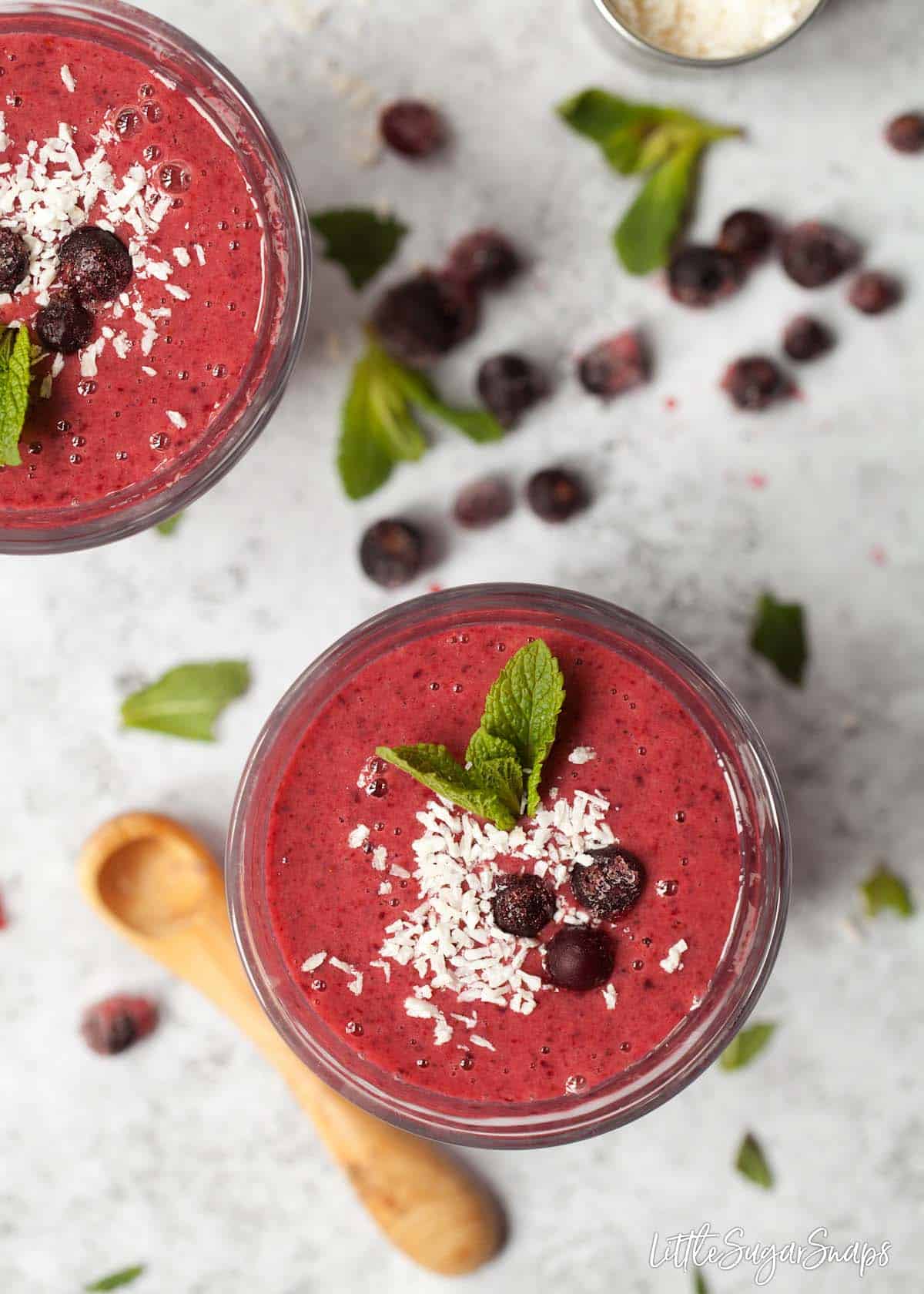 Glasses of blackcurrant smoothie topped with frozen blackcurrants, coconut and fresh mint