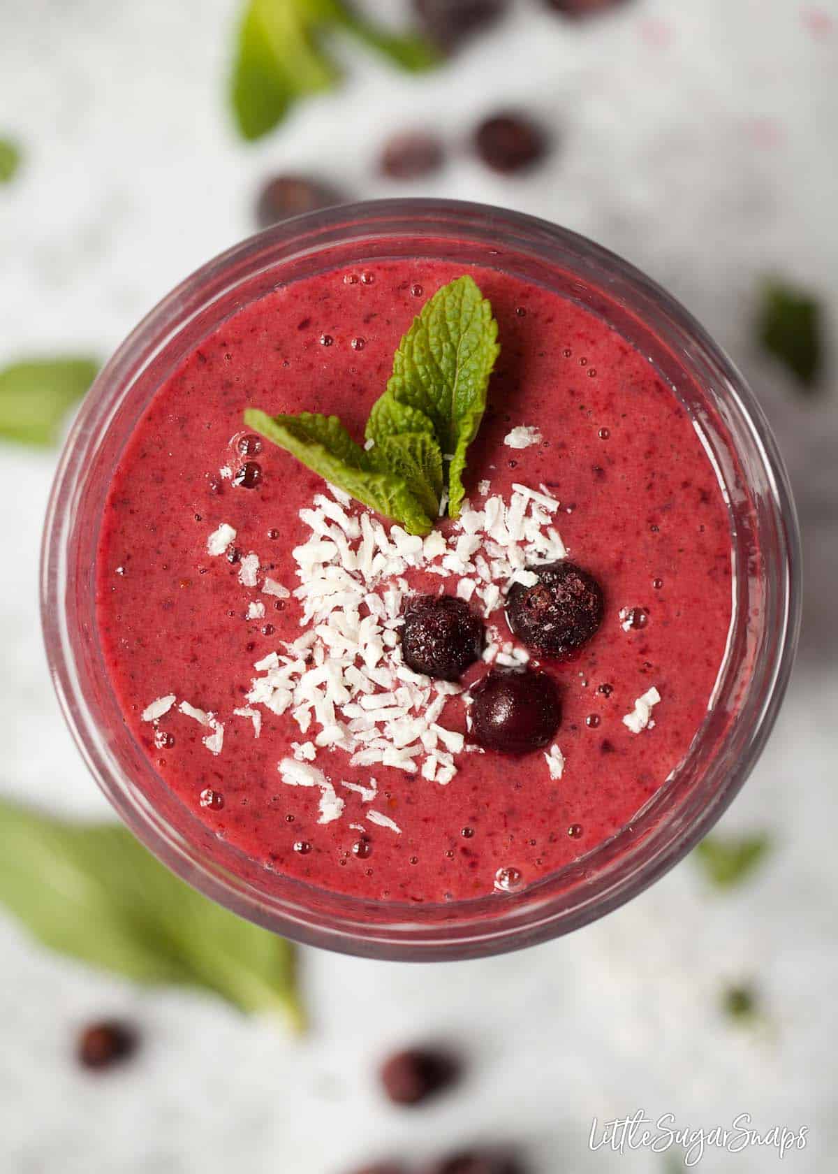 Close up view of blackcurrant smoothie topped with frozen blackcurrants, coconut and fresh mint