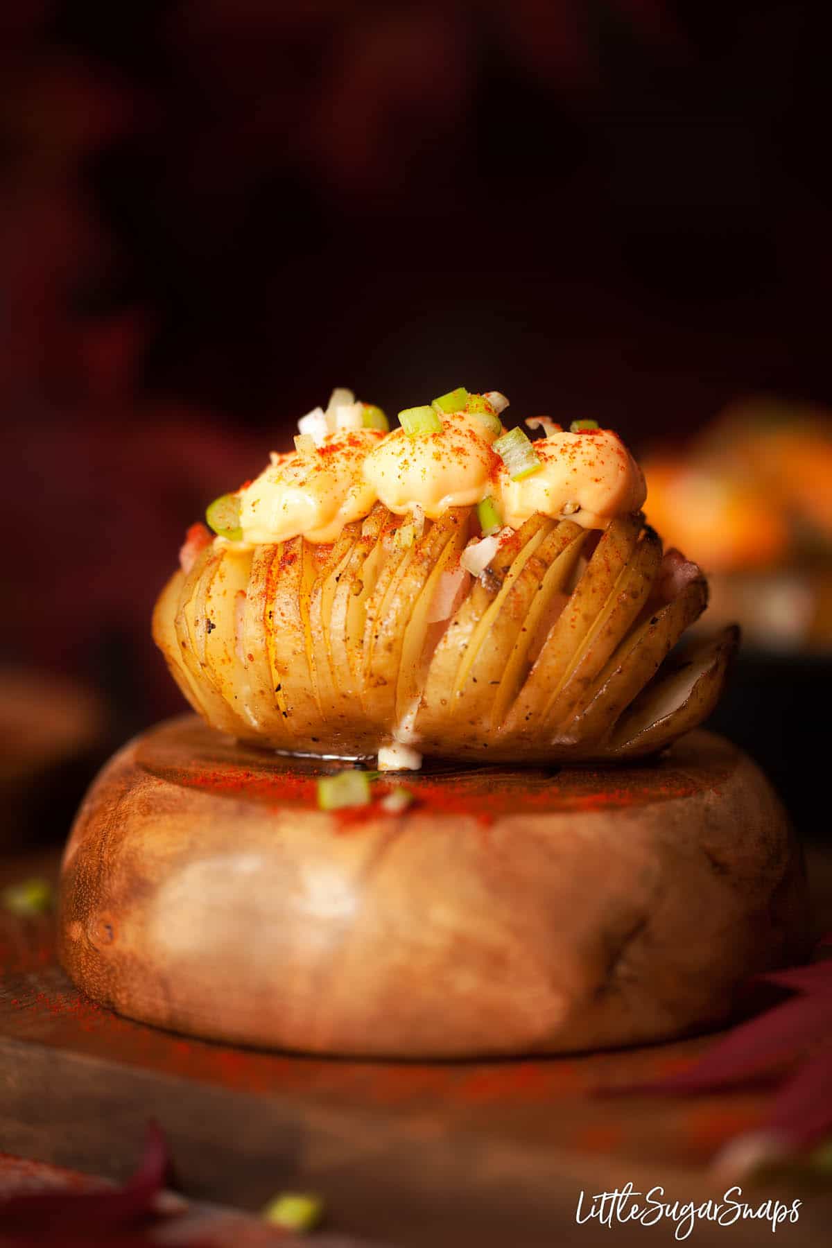 A cheesy hasselback potato filled with bacon sitting on an upturned wooden bowl.